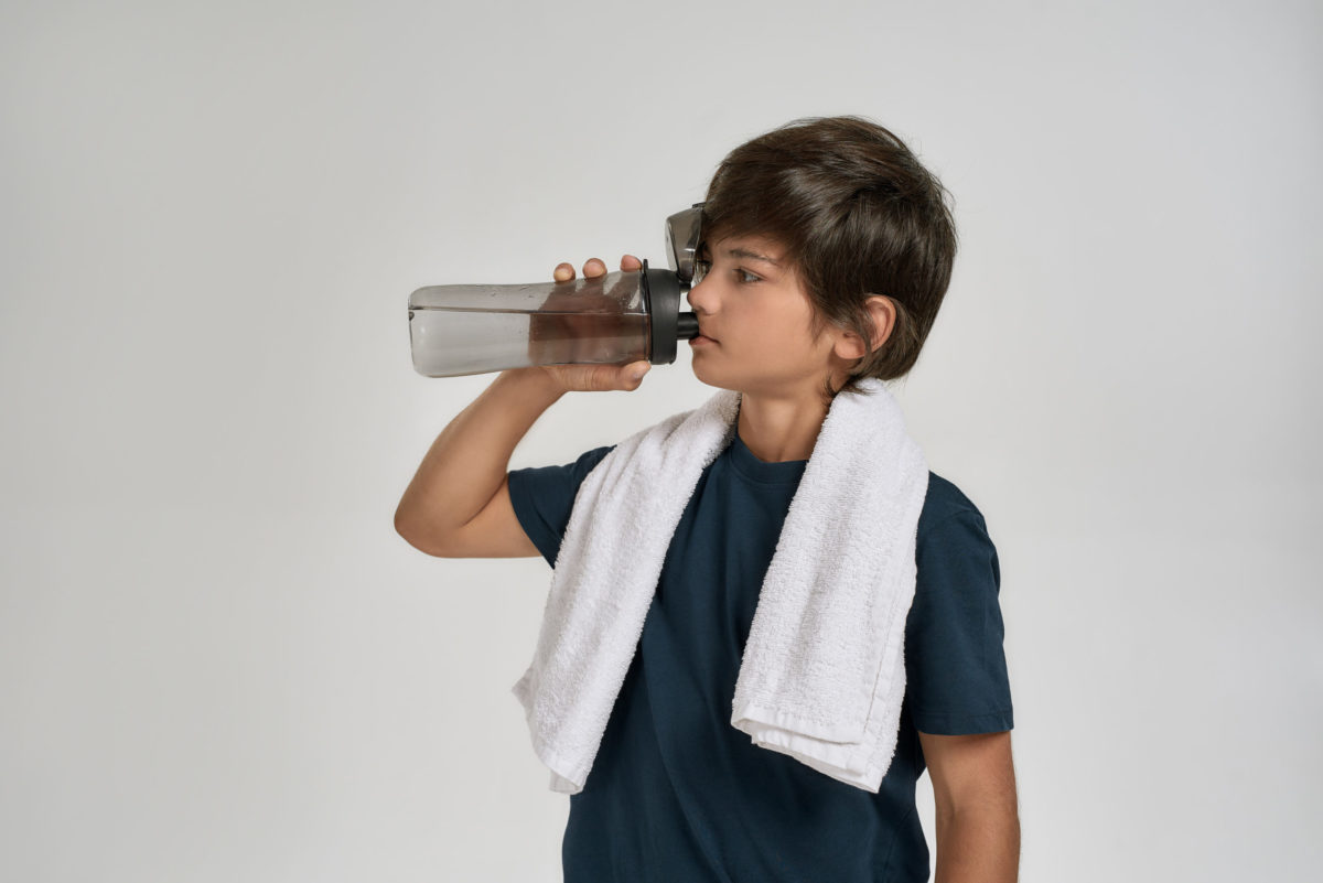 Young boy in sportswear drinking water from the bottle.