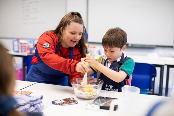 Child receives help stirring their mixture of ingredients in a bowl with an Activate helper