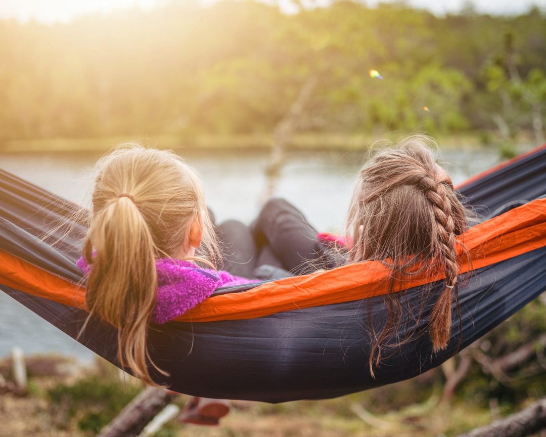 Making friends at holiday camp. Two girls sat on a hammock during dusk.